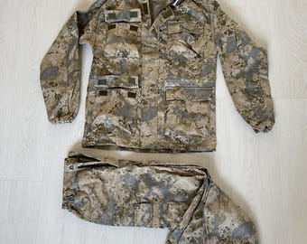 May include: A camouflage-patterned jacket and pants set. The jacket has a hood and multiple pockets. The pants have a drawstring waist and elastic cuffs.