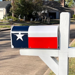 May include: A white mailbox with a Texas flag design. The mailbox is mounted on a white wooden post.