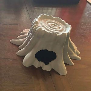 May include: A white, ceramic tree stump with a hollowed-out center. The stump has a rough, textured surface and a circular opening in the top.