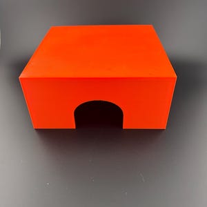 May include: A bright orange plastic box with a rounded arch opening in the front. The box is sitting on a dark gray surface.