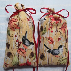 May include: Two fabric pouches with a fall-themed pattern featuring birds, leaves, and acorns. The pouches are tied with red ribbons. The background has a light wood grain appearance. The overall color scheme includes shades of brown, orange, and green.