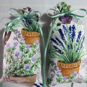 May include: Two white fabric sachets with green ribbon ties. The sachets feature a floral print of potted lavender and other herbs.