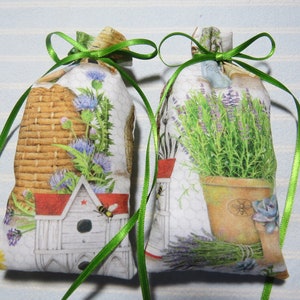 May include: Two fabric sachets with green ribbon ties. One sachet features a beehive, a birdhouse, and flowers. The other sachet features a potted lavender plant and lavender sprigs.