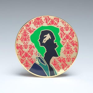 May include: A gold-colored round pin with a red and white patterned background. A green silhouette of a person's head with a smaller silhouette of a person falling inside the head.