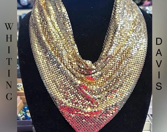 May include: A gold-toned chainmail necklace with a triangular shape. The necklace is made of small, interconnected metal rings.
