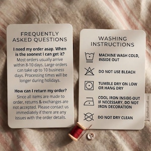 May include: Two white cards with rounded corners. One card reads "FREQUENTLY ASKED QUESTIONS" and the other reads "WASHING INSTRUCTIONS". A spool of red thread and a button are at the bottom. The cards provide care and order information.