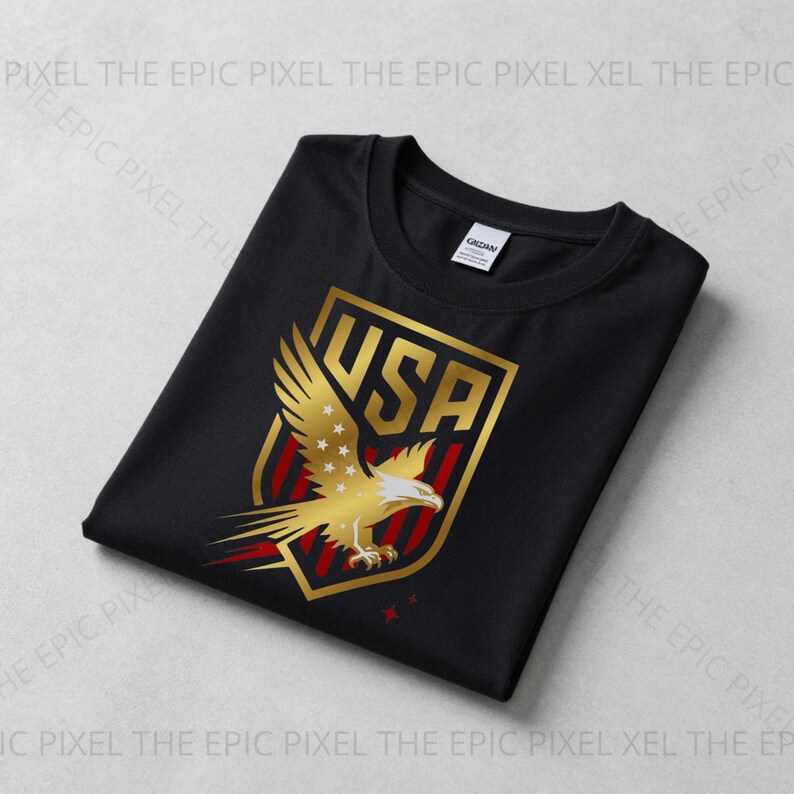May include: Black t-shirt featuring a gold and red USA emblem with an eagle design. The emblem includes the word "USA" and stars. The shirt is folded and displayed on a light gray surface.