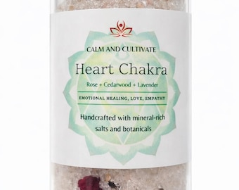 May include: A glass jar filled with Heart Chakra bath salts, featuring rose, cedarwood, and lavender. The label reads "CALM AND CULTIVATE" and "EMOTIONAL HEALING, LOVE, EMPATHY." The jar is topped with a wooden lid. The bottom text says "HEART CHAKRA BATH SALTS CRAFTED FOR JOY, SENSUALITY & INSPIRATION."