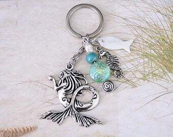 May include: Silver mermaid keychain with a blue and green glass bead, a white seashell fish charm, a silver seahorse charm, and a silver swirl charm.