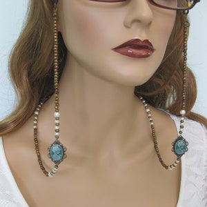 May include: A double-strand eyeglass chain with brown and white beads and two green cameo pendants.