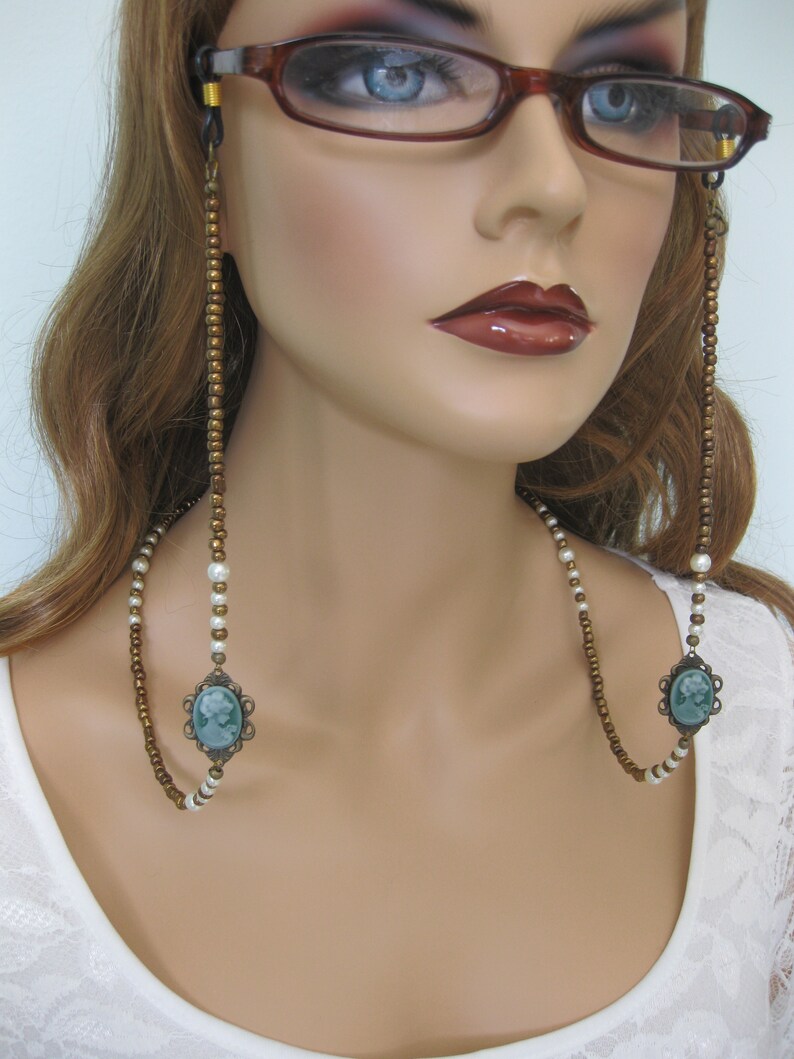 May include: A double-strand eyeglass chain with brown and white beads and two green cameo pendants.