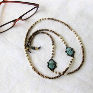 May include: A brown and white beaded eyeglass chain with two cameo pendants. The chain is made of small round beads and has a simple design.
