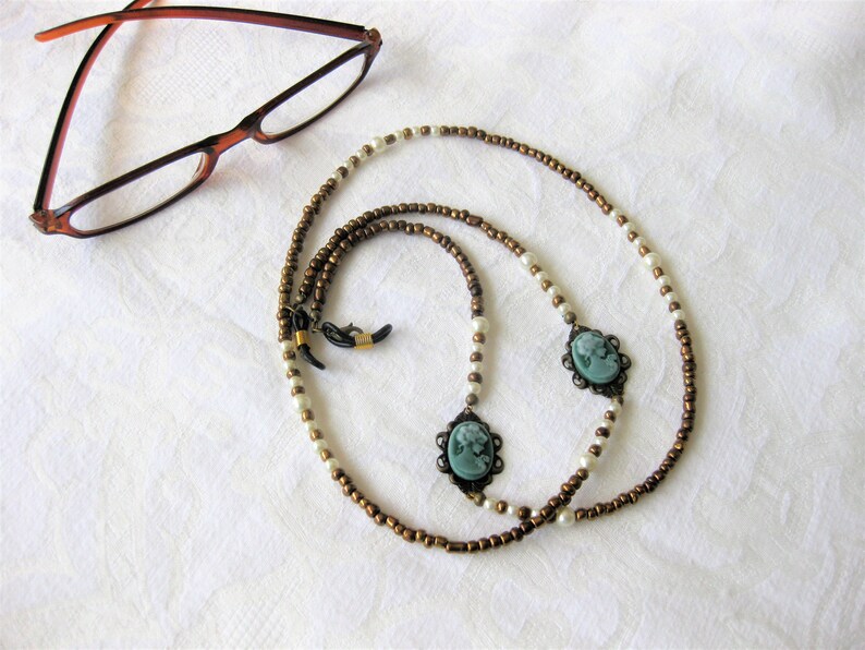 May include: A brown and white beaded eyeglass chain with two cameo pendants. The chain is made of small round beads and has a simple design.