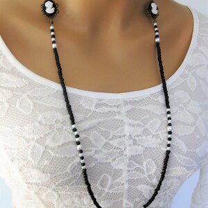 May include: A long black and white beaded necklace with two cameo pendants. The necklace is made of small black and white beads and features two antique-style cameo pendants.