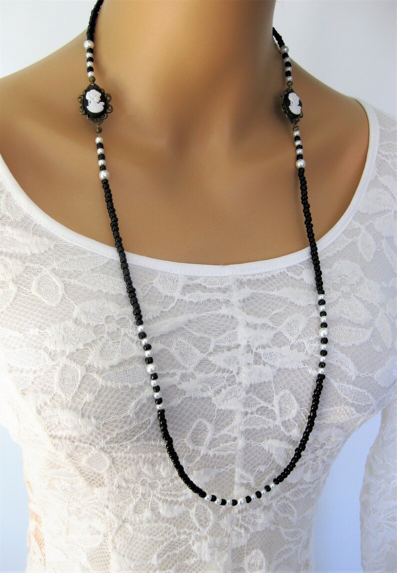 May include: A long black and white beaded necklace with two cameo pendants. The necklace is made of small black and white beads and features two antique-style cameo pendants.