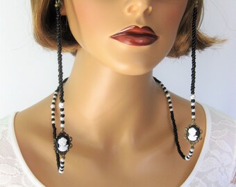 May include: Black and white beaded eyeglass chain with cameo charms. The chain is worn by a model with short brown hair and is attached to the temples of the glasses.