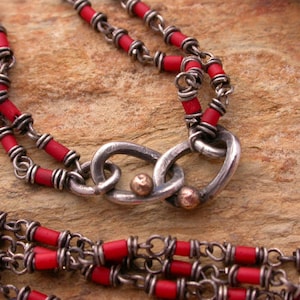 May include: A silver chain necklace with red beads and a silver clasp. The clasp is a double loop design with two small gold beads.