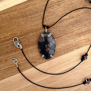 May include: A black cord necklace with a pink and black oval pendant and small pink glass beads.