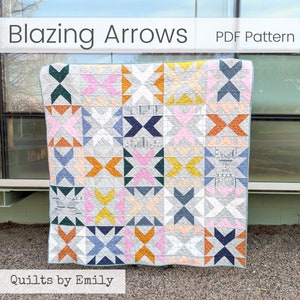 Op de afbeelding: Een quilt met een patroon van kleurrijke pijlen in tinten blauw, oranje, roze en geel op een grijze achtergrond. De quilt is getiteld "Blazing Arrows" en is gelabeld "PDF Pattern" en "Quilts by Emily".