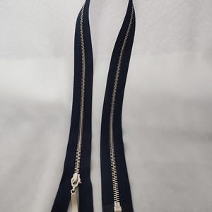 May include: Two navy blue zippers with silver metal teeth and pulls. The zippers are displayed against a white background. The zipper teeth are interlocked, and the pulls are rectangular.