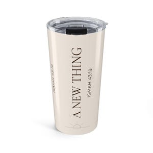 Op de afbeelding: Een beige roestvrijstalen beker met een doorzichtig plastic deksel en een zwarte schuifsluiting. De beker is voorzien van de donkerbruine tekst A NEW THING en ISAIAH 43:19 verticaal gedrukt, met een klein zon-icoon aan de onderkant van het ontwerp.