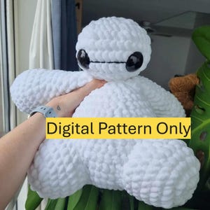 May include: White crocheted plush toy resembling a robot character with black eyes and a black line across the face. The toy is being held by a hand and the text "Digital Pattern Only" is visible in the image.