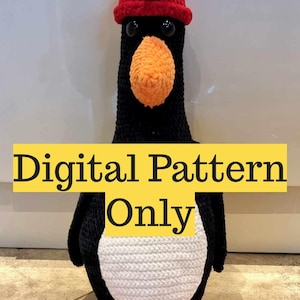 Puede incluir: Un pingüino de peluche hecho a mano, con cuerpo negro, vientre blanco y pico y patas naranjas. Lleva un sombrero rojo. El texto "Digital Pattern Only" se muestra en una pancarta amarilla.