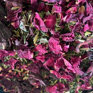 May include: A close-up of a blend of dried herbs and flowers, including rose petals, hibiscus, and green tea leaves. The mixture is a vibrant mix of red, pink, and green.