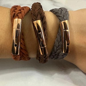 Può includere: Tre braccialetti in pelle intrecciata con chiusura dorata. I braccialetti sono marroni, beige e grigi.