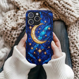 Puede incluir: Funda de teléfono con un diseño de vidriera que representa una luna creciente dorada y estrellas sobre un fondo azul oscuro. La funda tiene un parachoques protector. El diseño incluye tonos dorados, azules y amarillos.