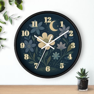 May include: A round wall clock with a black frame. The clock face is dark blue with floral and celestial designs, including flowers, a crescent moon, and stars. The numbers are gold, and the hands are white.