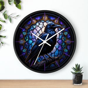 Puede incluir: Un reloj de pared redondo negro con una ilustración detallada de un cuervo negro posado en una rama. El cuervo se encuentra sobre un fondo de estilo vidriera con tonos azules, morados y dorados. El reloj tiene manecillas blancas y marcadores de hora morados.
