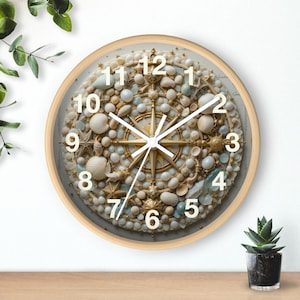 May include: A round wall clock with a light wood frame. The clock face is decorated with seashells, pearls, and a gold compass design. White numerals mark the hours, and the hands are gold.
