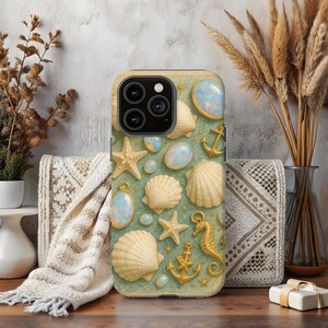 May include: A phone case with a sea-themed design. The case features seashells, starfish, opalescent gems, and gold anchors and seahorses on a light green background. The case has a camera bump and a light beige border.