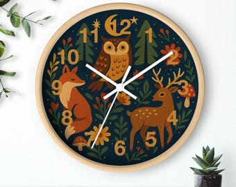 Könnte beinhalten: Eine runde Wanduhr mit hellem Holzrahmen. Das Zifferblatt hat einen dunkelblauen Hintergrund mit Illustrationen eines Fuchses, einer Eule und eines Hirsches. Die Zahlen sind in einer verspielten Schriftart, und die Zeiger sind weiß.