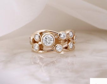 May include: A gold ring with multiple clear, round gemstones. The ring has a unique design with the gemstones set in a flowing, openwork pattern. The ring is displayed on a marble surface.
