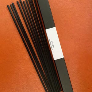 May include: A black box of diffuser reeds with the text "ENGLAND 30cm Diffuser Reeds" printed on the side.