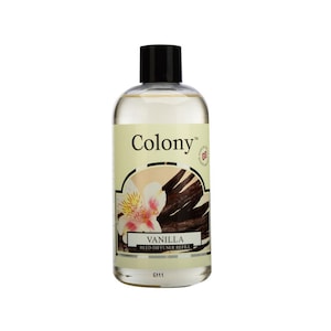 May include: A clear glass bottle with a black cap filled with a light yellow liquid. The bottle has a label with the text "Colony" and "Vanilla Reed Diffuser Refill" in black text on a cream background. The label also features a floral design and vanilla beans.