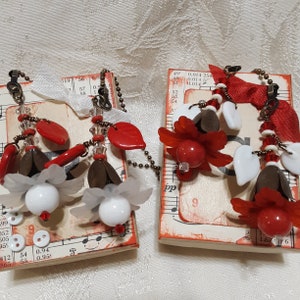 May include: Two small red and white decorated journals with a musical theme. Each journal has a red, white, and brown beaded chain with red and white beads and a red leaf charm.