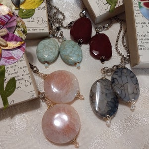 May include: A set of six agate stone earrings with silver and gold chains. The earrings feature different colors and patterns, including light blue, pink, and gray.