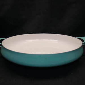 May include: A teal enamel pan with a white interior and two curved handles. The oval-shaped pan is designed for cooking. The pan is approximately 30 cm in diameter.