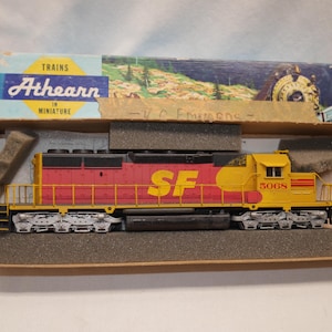 May include: A model diesel locomotive train in a cardboard box. The train is painted red and yellow with the letters SF and the number 5068 on the side. The box features the text Trains Athearn in Miniature and a landscape illustration.