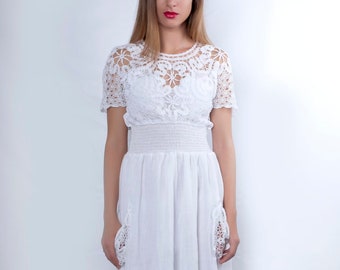May include: A white crochet dress with a lace bodice and a flowing skirt. The dress has a fitted bodice and a loose-fitting skirt. The model is wearing the dress with nude heels.