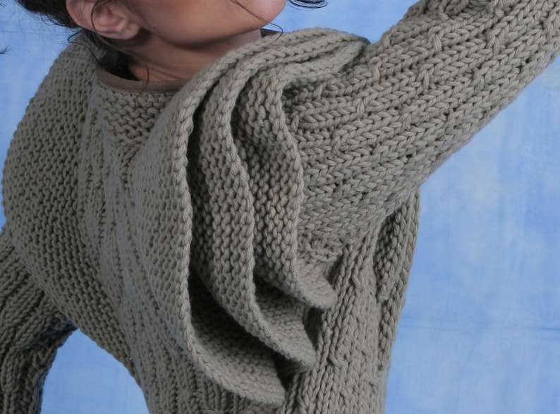 May include: A grey knitted sweater with a unique draped design. The sweater is made from a soft, textured yarn and has a relaxed fit.