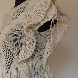 May include: A white crocheted top with a ruffled neckline and a delicate openwork pattern. The top has a fitted bodice and a loose, flowing skirt.