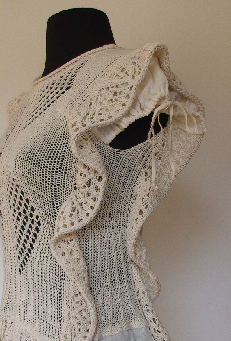 May include: A white crocheted top with a ruffled neckline and a delicate openwork pattern. The top has a fitted bodice and a loose, flowing skirt.