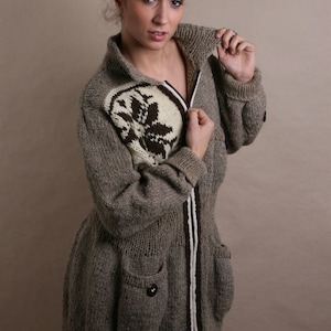 May include: A long, gray knitted cardigan with a white and brown patterned design. The cardigan has a zipper closure and two pockets.