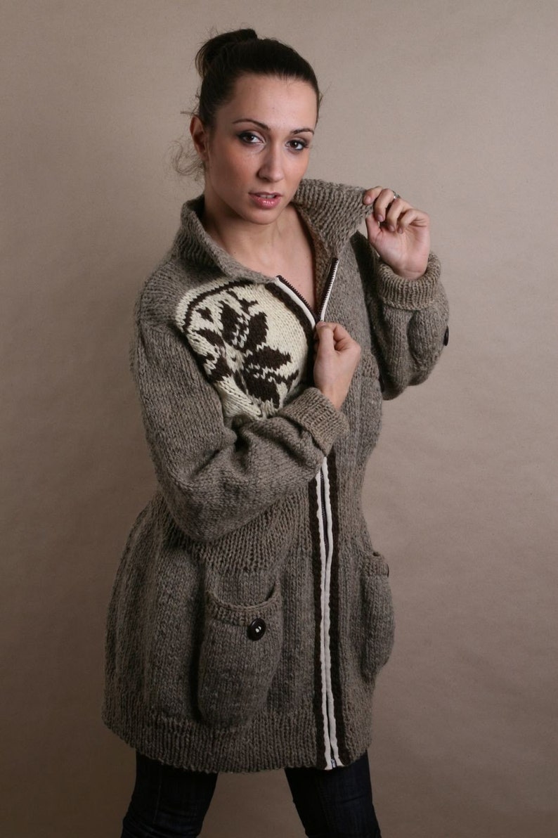 May include: A long, gray knitted cardigan with a white and brown patterned design. The cardigan has a zipper closure and two pockets.