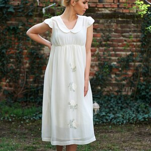 May include: A white dress with a Peter Pan collar and embroidered flowers. The dress is knee-length and has a fitted bodice and a flowing skirt.