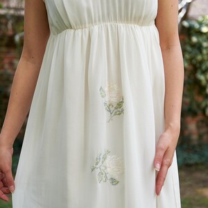 May include: A white sleeveless dress with a Peter Pan collar and embroidered white roses.